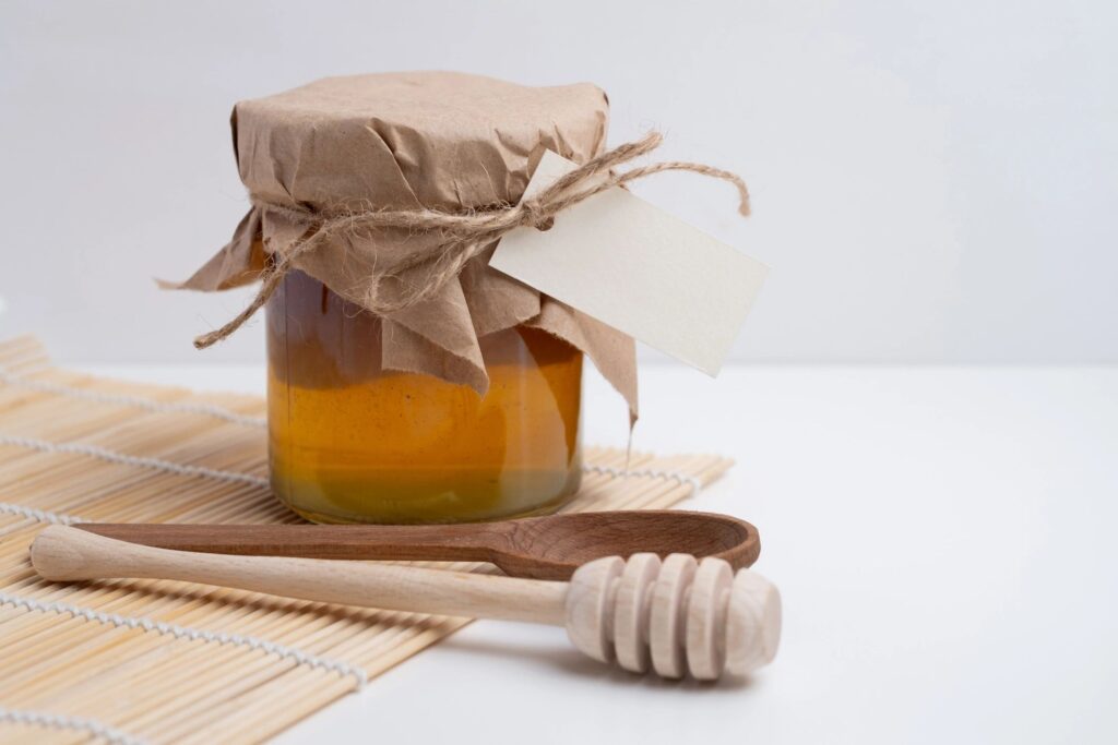 Jar of honey with wooden honey dipper on white kitchen background. Tasty honey bunker.